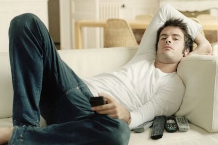 Man Relaxing On Sofa Holding Remote Controls